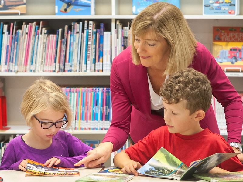 librarian looking at a book with students librarian looking at a book with students